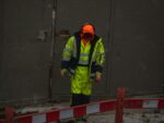 man in green jacket and orange helmet standing on gray concrete floor