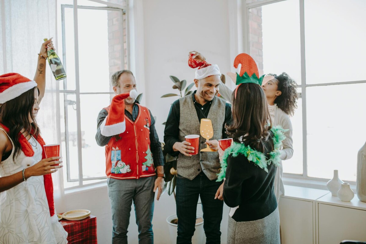 Colleagues celebrating a festive holiday party in an office setting, enjoying drinks and wearing fun costumes.