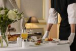 A luxurious hotel room showcasing an elegant room service breakfast setup with fresh flowers and a platter of assorted pastries.