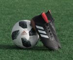 black adidas cleats lean on white and black adidas soccer ball on green grass